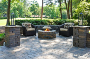 A beautiful outdoors pavers with two comfortable armchairs and a fire pit in a natural green environment